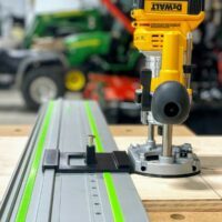 DeWalt plunge router mounted on gray rail with green edge guide, positioned above holes drilled in wood