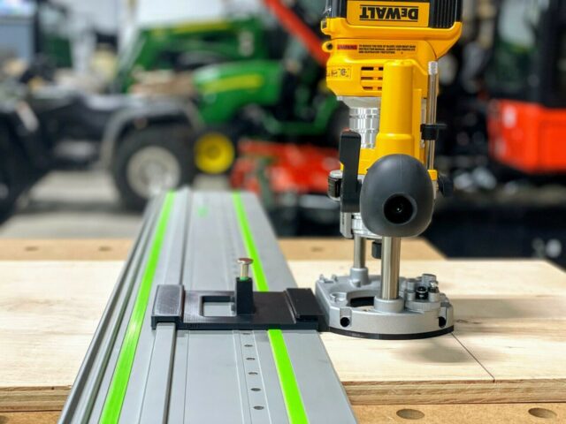 DeWalt plunge router mounted on gray rail with green edge guide, positioned above holes drilled in wood