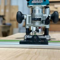 Makita plunge router mounted on ToolCurve LR32 plate attached to Festool guide rail, front view showing black adapter base and adjustment knobs