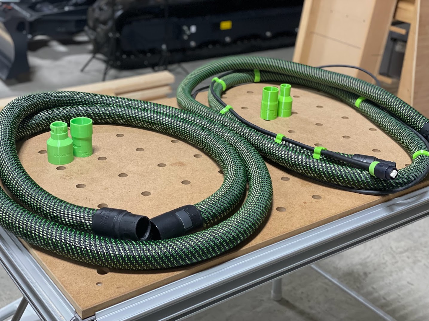 Green and black hose connectors and adapters displayed on a perforated work surface, showing various port sizes for Festool dust extraction systems.