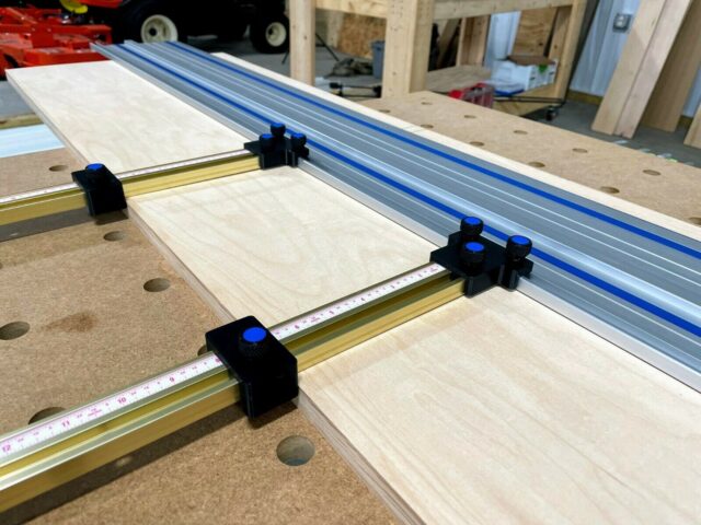 Black plastic parallel guide brackets with blue knobs mounted on brass rails attached to a Kreg ACS track saw guide rail system