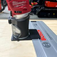 Milwaukee M18 trim router mounted on black adapter plate attached to Bosch guide rail on wooden workbench