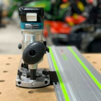 Makita trim plunge router mounted on ToolCurve LR32 adapter, positioned above an aluminum guide rail with bright green edges
