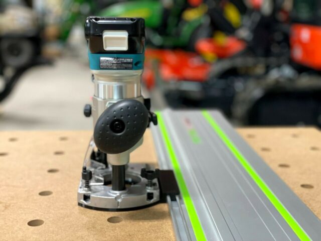 Makita trim plunge router mounted on ToolCurve LR32 adapter, positioned above an aluminum guide rail with bright green edges