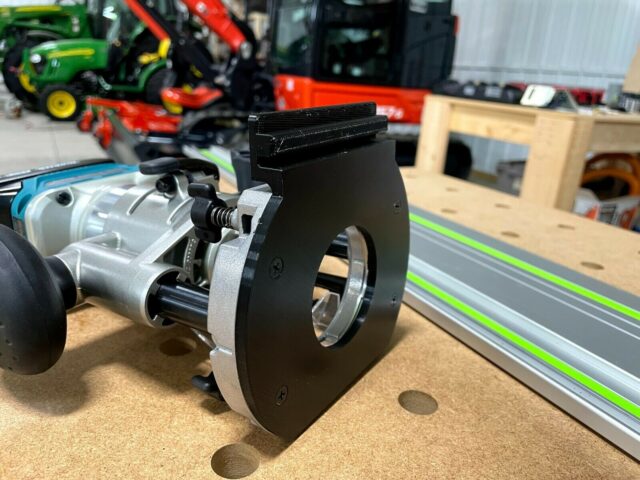 Black plastic adapter mounted on a Makita trim plunge router, shown attached to an aluminum guide rail with green stripe