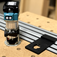 Makita trim router mounted on black adapter plate positioned on Dewalt track saw aluminum track over perforated wooden base