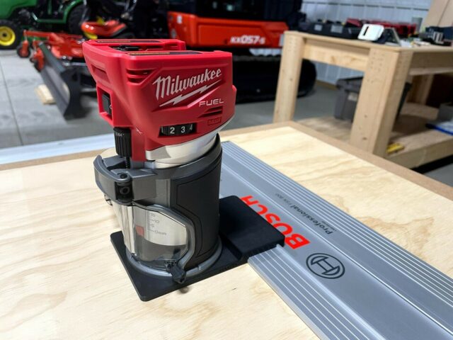 Milwaukee M18 trim router mounted on black adapter base sitting on a Bosch guide rail