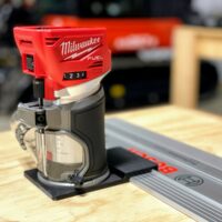 Milwaukee M18 Fuel trim router on a black guide rail adapter base, riding a Bosch rail on plywood