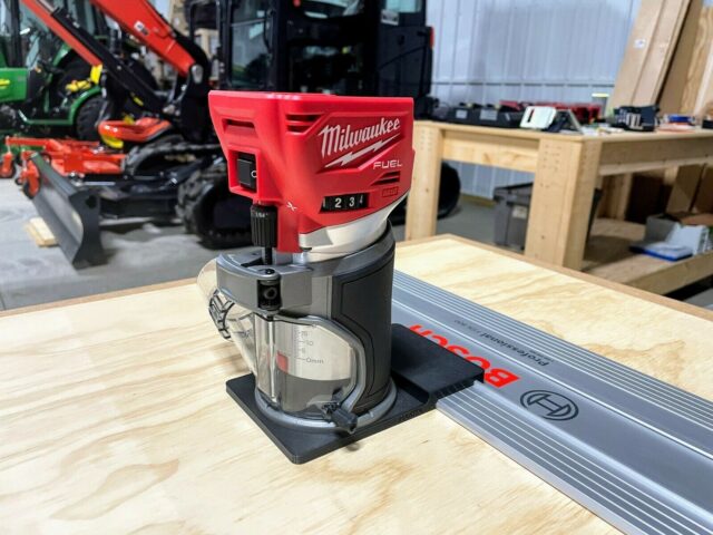 Milwaukee M18 trim router mounted on black plastic adapter base, positioned on Mafell aluminum guide rail