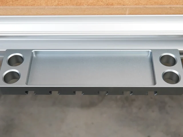 Aluminum utility rack with central tray and four mounting holes for clamps, mounted on workbench t-track