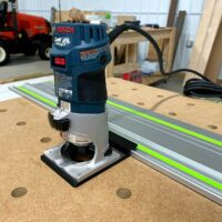 Bosch Colt 1HP router mounted on an aluminum guide rail with bright green stripe, white base adapter connecting router to rail