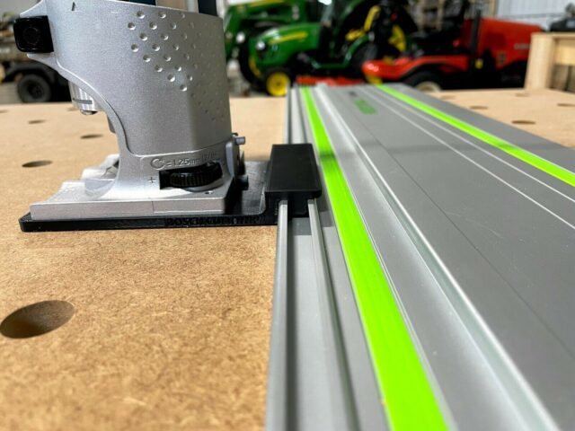 Bosch Colt 1HP router adapter mounted on a Festool guide rail, showing the silver adapter body with perforated face and black mounting bracket engaged with the rail