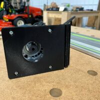 Black 3D-printed adapter plate with mounted Bosch router base, threaded mounting holes visible, positioned next to Festool guide rail on workbench