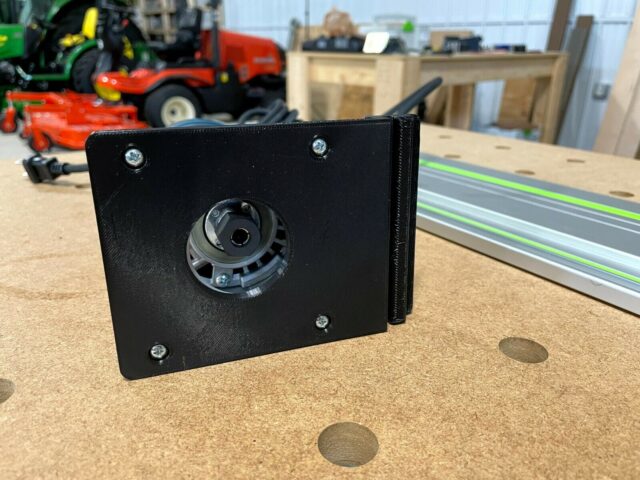 Black 3D-printed adapter plate with mounted Bosch router base, threaded mounting holes visible, positioned next to Festool guide rail on workbench