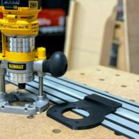 Dewalt plunge router attached to Dewalt track saw track, showing black adapter base mounted on aluminum rail with guide holes