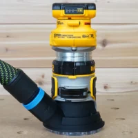 Black hose adapter with blue band attached to DeWalt DCW600 compact router base, showing dust collection port connection