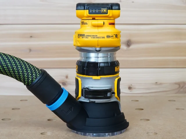 Black hose adapter with blue band attached to DeWalt DCW600 compact router base, showing dust collection port connection
