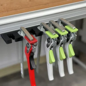 Black quick clamp holder mounted in a workbench t-track profile with one red and three green clamps hanging