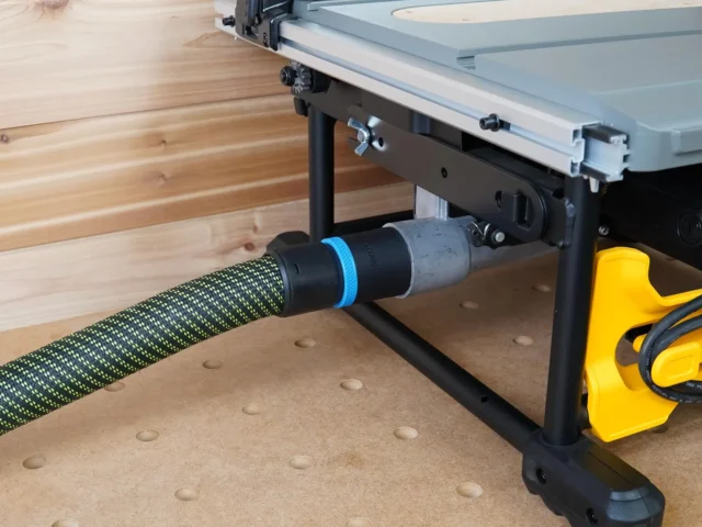 Black 36mm hose adapter with blue ring joining a green vacuum hose to a Dewalt table saw's rear dust port