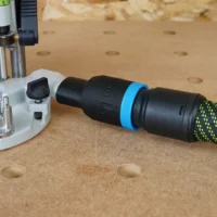 Black hose adapter with blue band attached to Festool 1010 router, connected to green and yellow braided 27mm hose on pegboard workbench