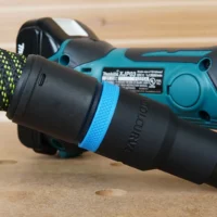 Black hose adapter with blue identification band attached to Makita plate joiner dust port, with yellow-green braided hose connected