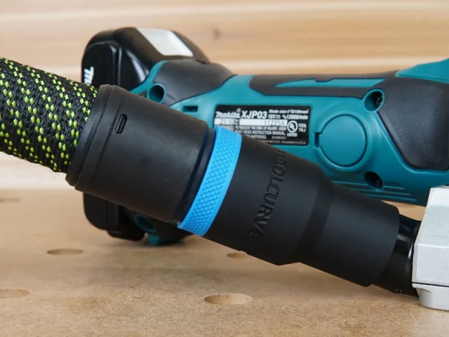 Black hose adapter with blue identification band attached to Makita plate joiner dust port, with yellow-green braided hose connected