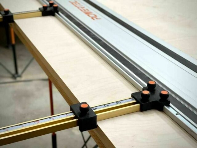 Two black parallel guide brackets with orange knurled knobs mounted on brass Incra T-Track rails attached to a PowerTec track saw rail.