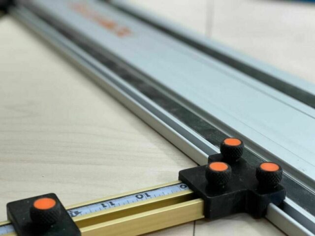 Black parallel guide brackets with orange knobs mounted on a PowerTec track saw rail, positioned on a workbench