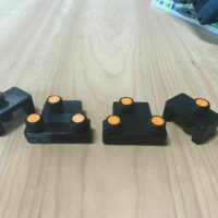 Four black 3D-printed parallel guide brackets with orange knurled knobs, arranged in a row on a light wood surface