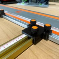 Black 3D-printed parallel guide with three orange knurled knobs, mounted on a brass Incra T-Track rail next to a Wen track saw guide