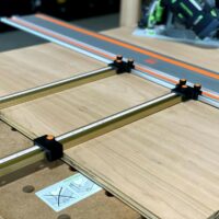Black parallel guide brackets with orange knobs mounting Incra T-Tracks to a Wen guide rail on plywood