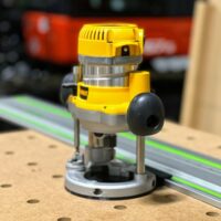 DeWalt DW618 plunge router mounted on a green guide rail using the ToolCurve adapter base, shown on a work surface with a router in the background
