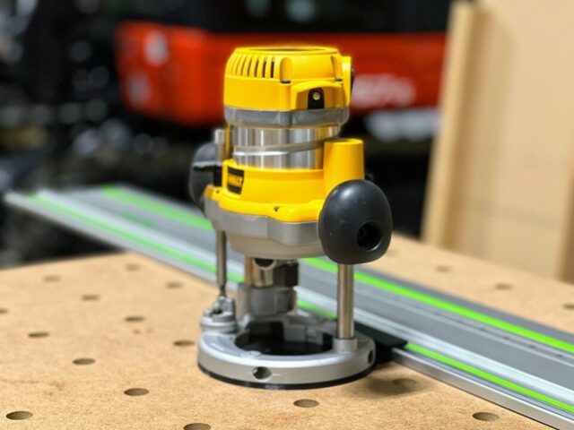 DeWalt DW618 plunge router mounted on a green guide rail using the ToolCurve adapter base, shown on a work surface with a router in the background