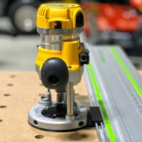 DeWalt DW618 plunge router mounted on a Festool guide rail adapter, seated on a wooden board with alignment holes