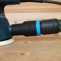 ToolCurve hose adapter attached to Bosch orbital sander dust port, black plastic with blue band, connected to yellow-green braided hose