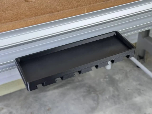 Black tray mounted in a Festool MFT/3 workbench t-track, with notched slots along the side for holding clamps and a flat storage area