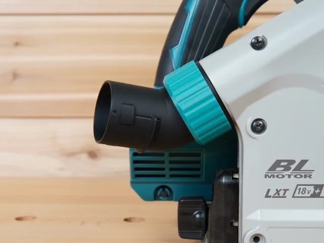 Turquoise twist-lock hose adapter connected to black dust port on Makita track saw, angled upward away from the cut area