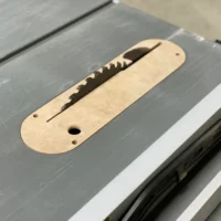 Light wood MDF zero clearance insert seated in Dewalt table saw throat, with slot for blade and mounting holes visible