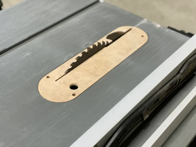 Light wood MDF zero clearance insert seated in Dewalt table saw throat, with slot for blade and mounting holes visible