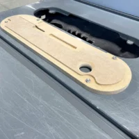 Tan MDF zero clearance insert for Dewalt table saw, shown installed in saw slot with black dust collection shroud visible behind it