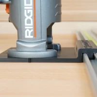 Ridgid trim router mounted on black plastic guide rail adapter, positioned over wooden workpiece with green and gray rails visible