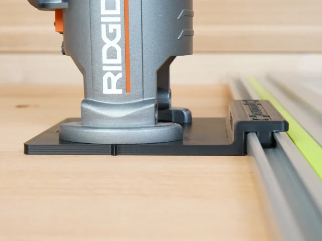 Ridgid trim router mounted on black plastic guide rail adapter, positioned over wooden workpiece with green and gray rails visible