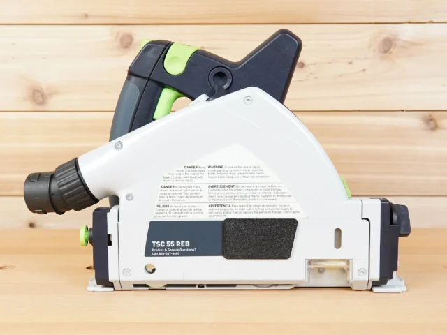 ToolCurve track saw arbor dust cover attached to Festool TS 55, white with black lever and green accents, shown from above on wooden surface