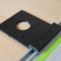 Black plastic adapter with central circular opening, mounted on aluminum guide rail with green stripe, showing mounting holes and embossed text on side block