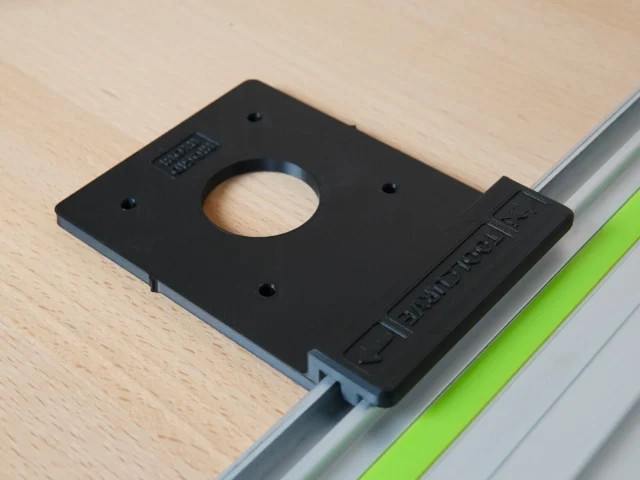 Black plastic adapter with central circular opening, mounted on aluminum guide rail with green stripe, showing mounting holes and embossed text on side block