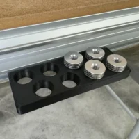 Black PLA Plus MFT bench dog holder in the workbench t-track, four metal dogs in eight round slots