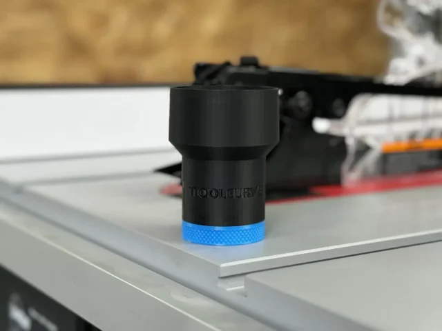 Black hose adapter with blue grip band sitting on a SawStop table saw dust port, ToolCurve branding visible