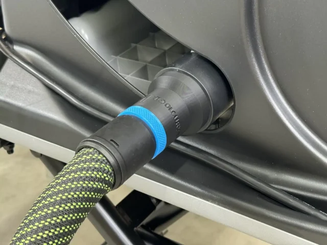 Black hose adapter with blue collar attached to SawStop table saw dust port, connected to yellow-and-black braided hose