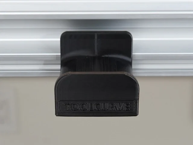 Black ToolCurve headphone holder clipped to Festool MFT/3 table t-track, front view showing dual compartments and branded nameplate
