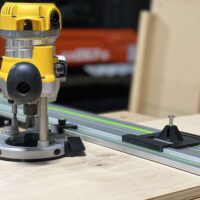 DeWalt DW618 plunge router mounted on LR 32 rail with black adapter plate and spring-loaded knob, positioned on Festool track